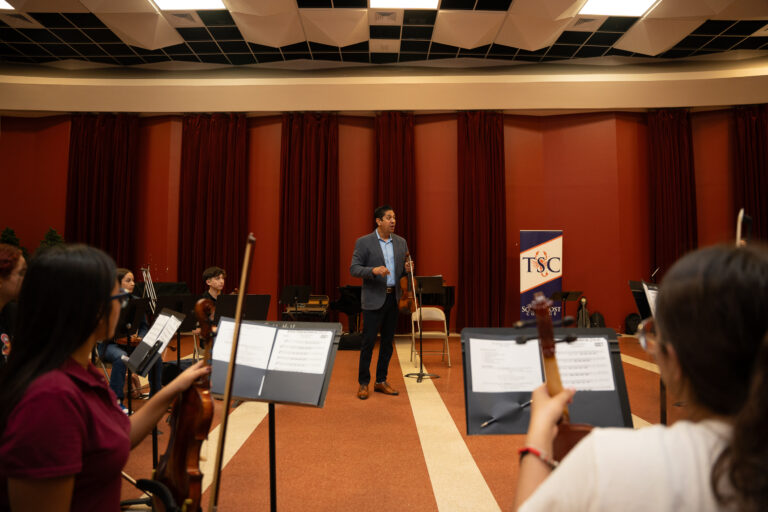 Master Class Conductor Adrian Vaca, a member of Mariachi Sol de Mexico de Jose Hernandez, guides student violinists in a lesson as part of the Mariachi Summer Camp, held at the TSC Performing Arts Center.
