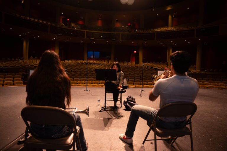 Trumpet students practicing with sheet music on stage at the TSC Performing Arts Center as part of the Mariachi Summer Camp.