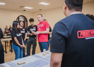 A volunteer mentor coaches his team of students during an interactive board game exercise as part of the Project Pipeline Summer Architecture Camp.
